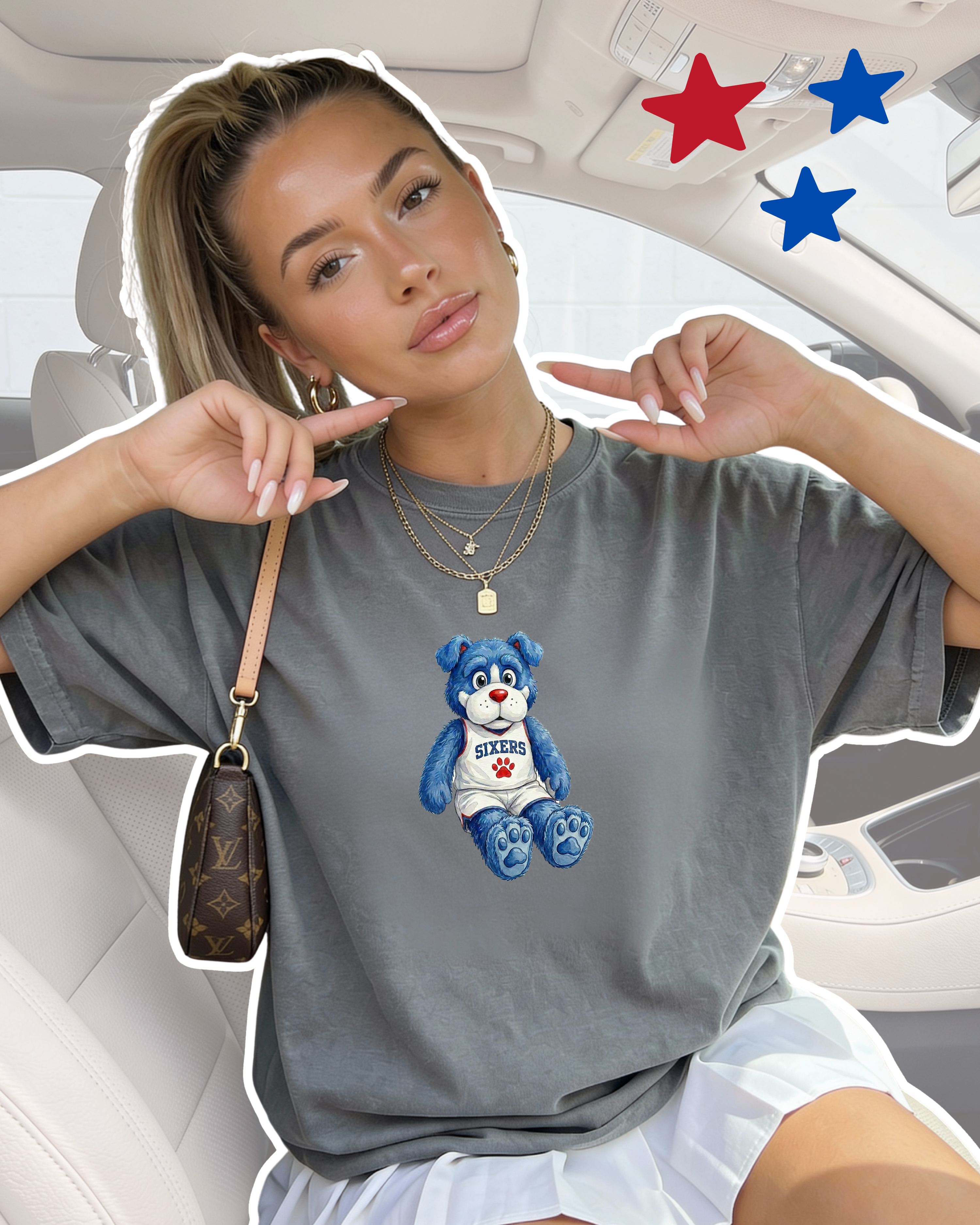 Woman sitting in a car wearing an oversized grey Comfort Colors t-shirt featuring a Sixers plushie graphic — a blue teddy bear in a white Sixers jersey with a red paw print, styled with layered gold necklaces and a mini Louis Vuitton bag.