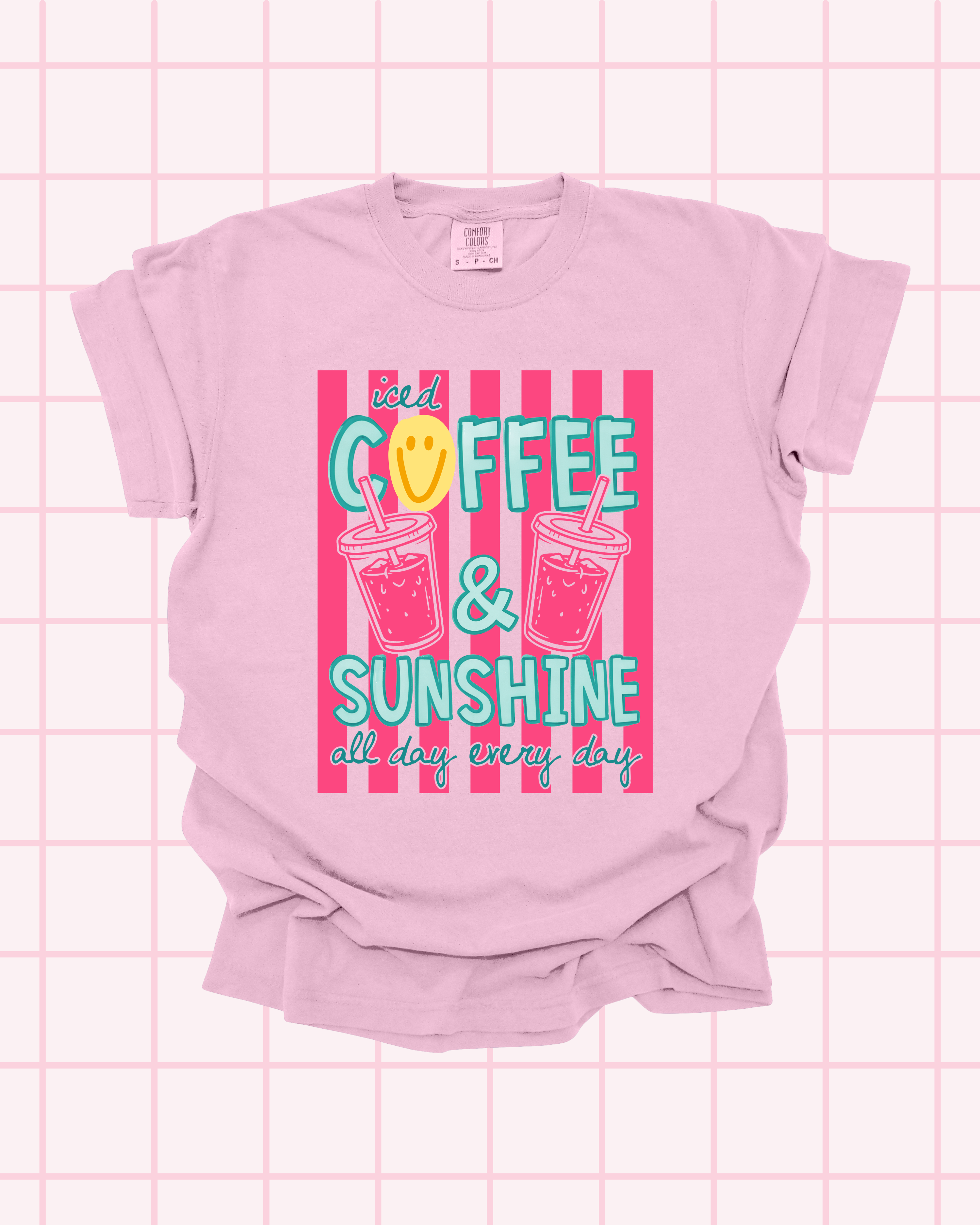 Flat lay of a blossom pink Comfort Colors t-shirt with "Iced Coffee & Sunshine, All Day Every Day" graphic in teal and pink, featuring illustrated iced coffee cups and smiley face accent by Santi Design Co.