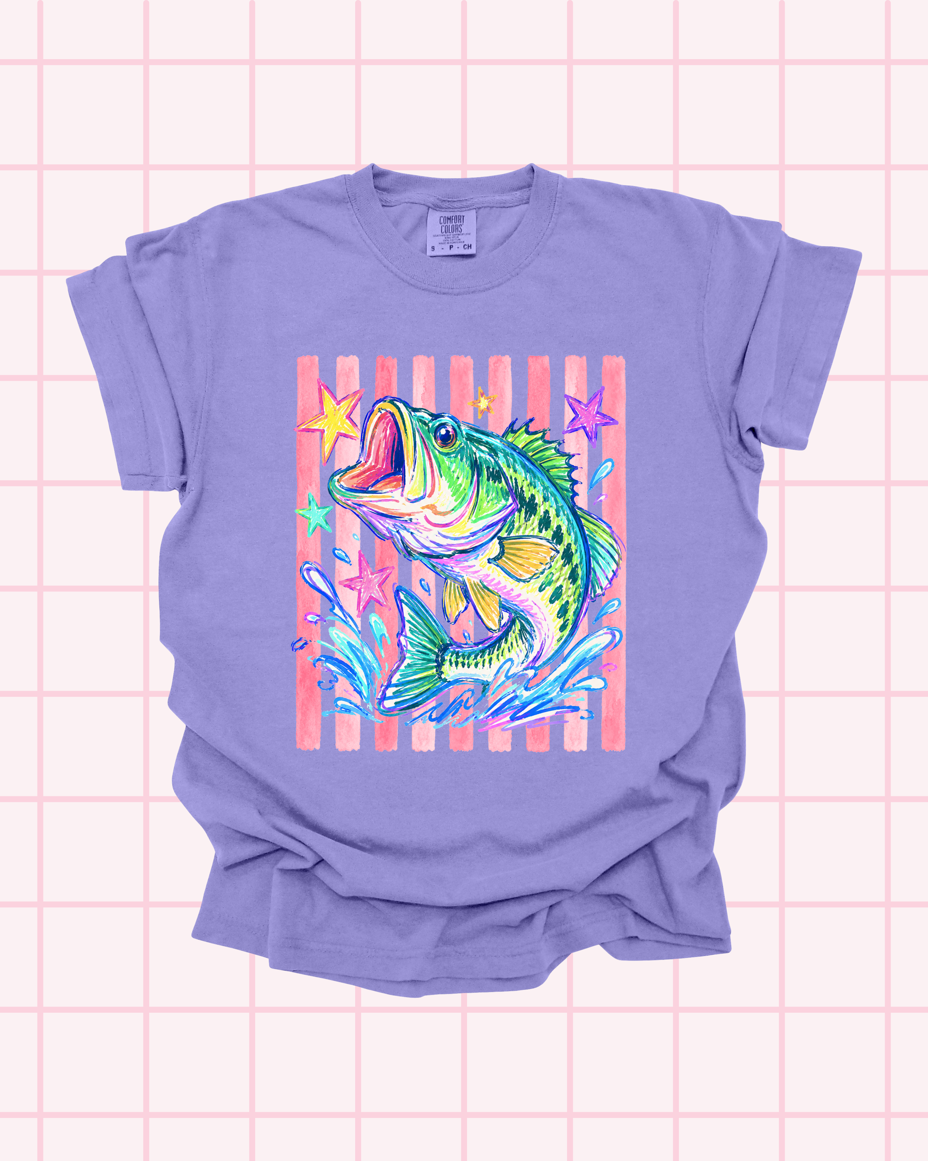 Flat lay of a violet Comfort Colors t-shirt featuring a vibrant hand-illustrated bass fish graphic with pink striped background and stars by Santi Design Co.