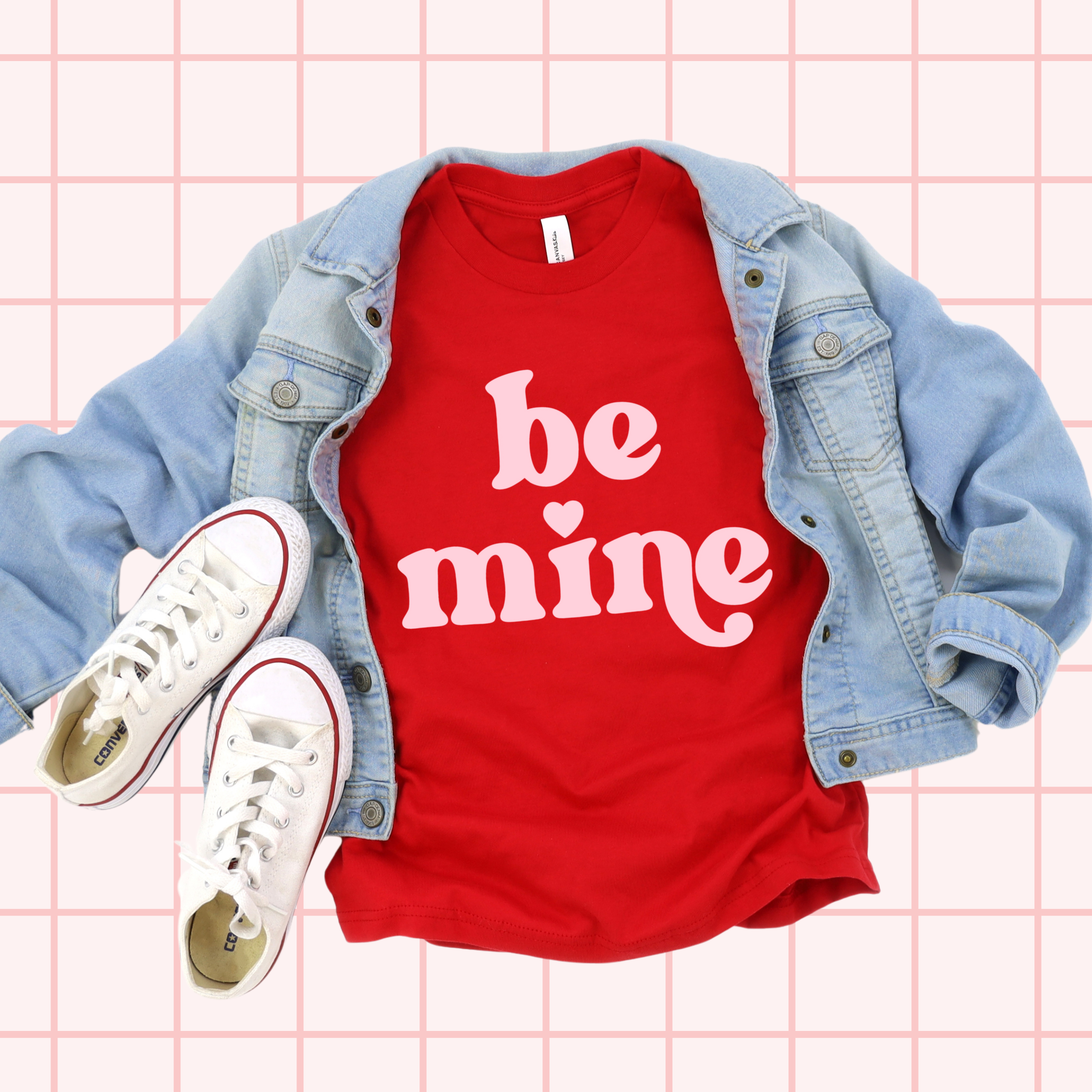 Red t-shirt with 'be mine' text, denim jacket, and white sneakers on a grid background