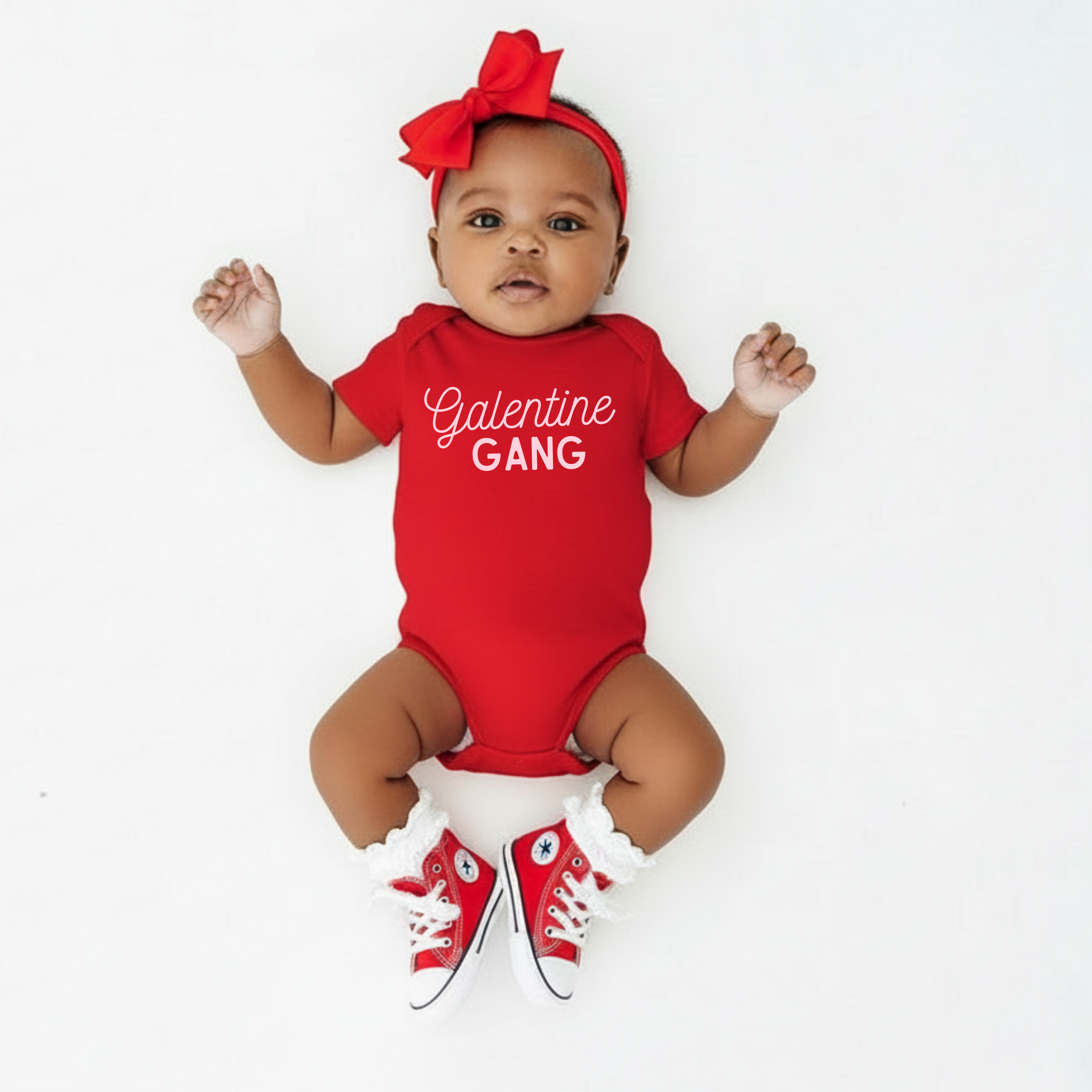 Baby wearing a red 'Galentine Gang' onesie with matching shoes and headband on a white background