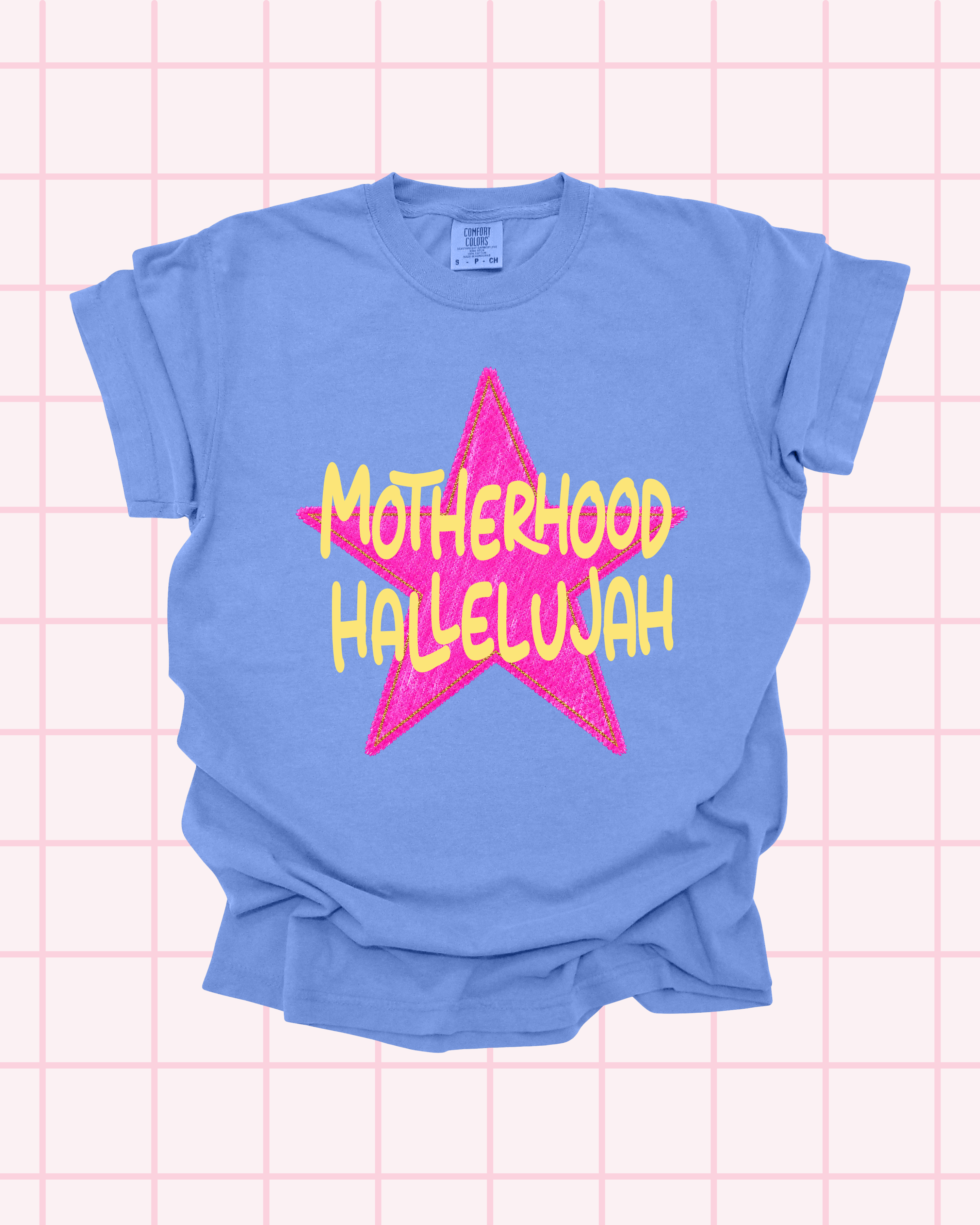 Flat lay of a flo blue Comfort Colors t-shirt with a bold pink star graphic featuring "Motherhood Hallelujah" in yellow lettering by Santi Design Co.