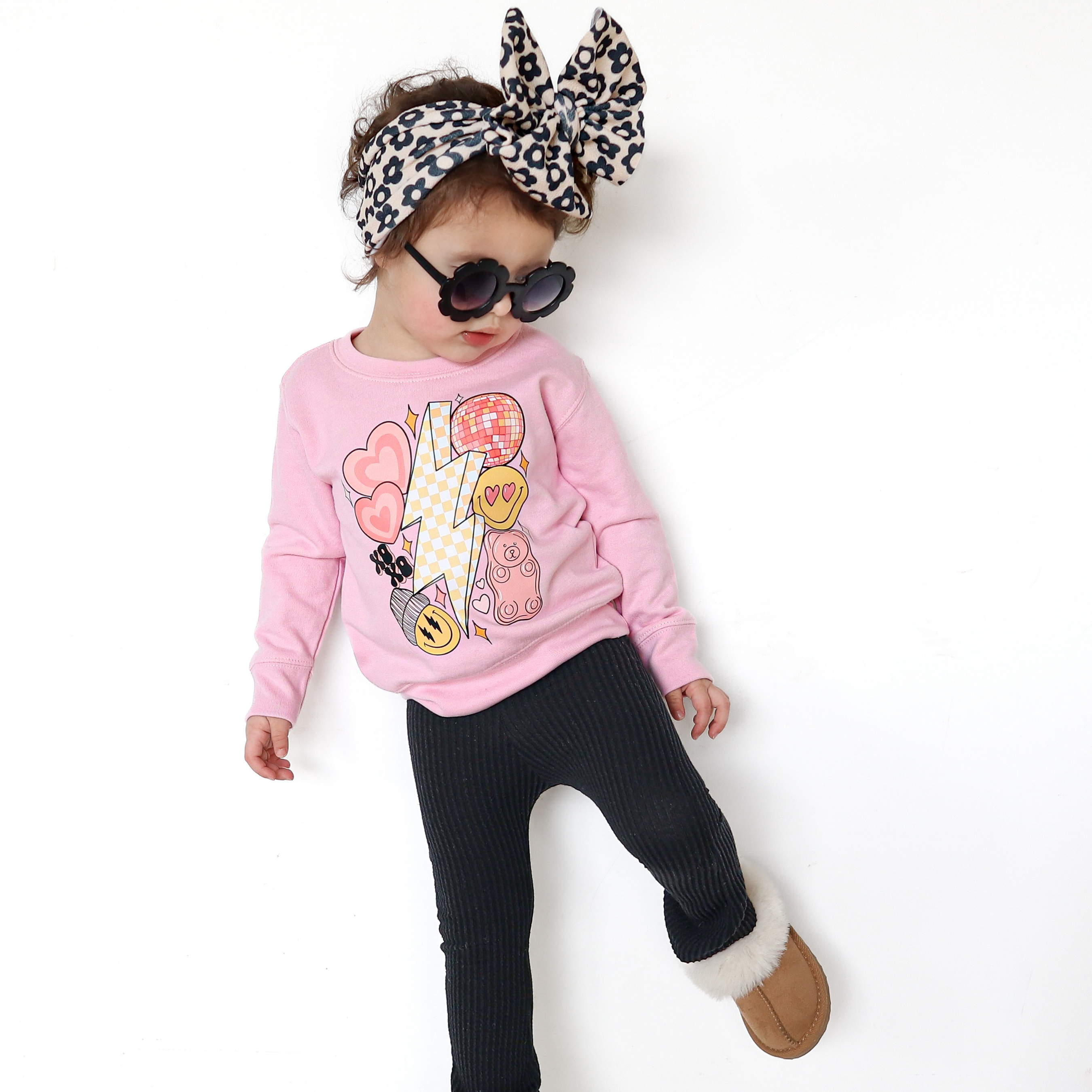 Child wearing a pink sweatshirt with Valentine's Day graphics, black pants, and sunglasses on a white background