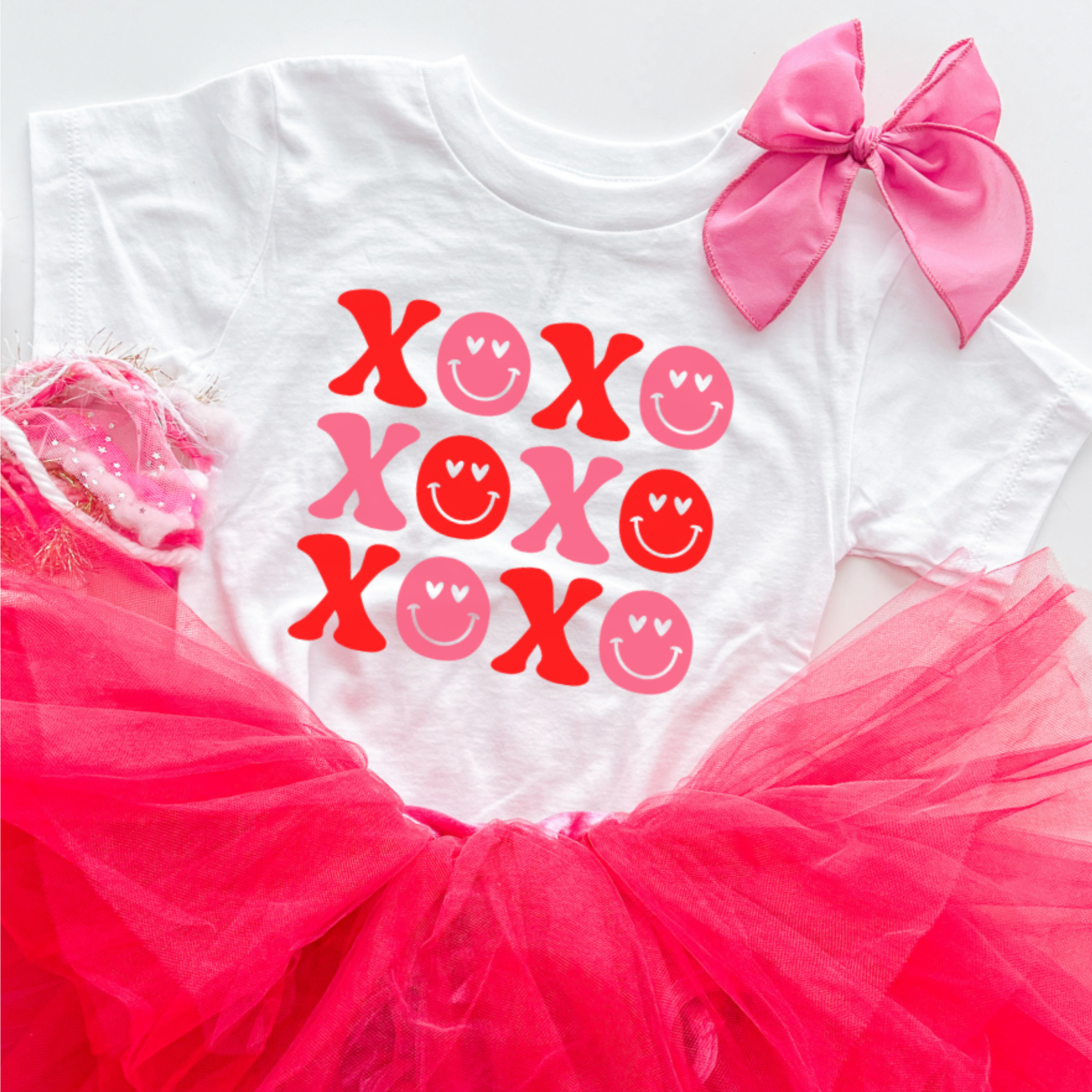 White shirt with pink and red 'XOXO' and smiley face designs, pink bow, and pink tutu on a white background