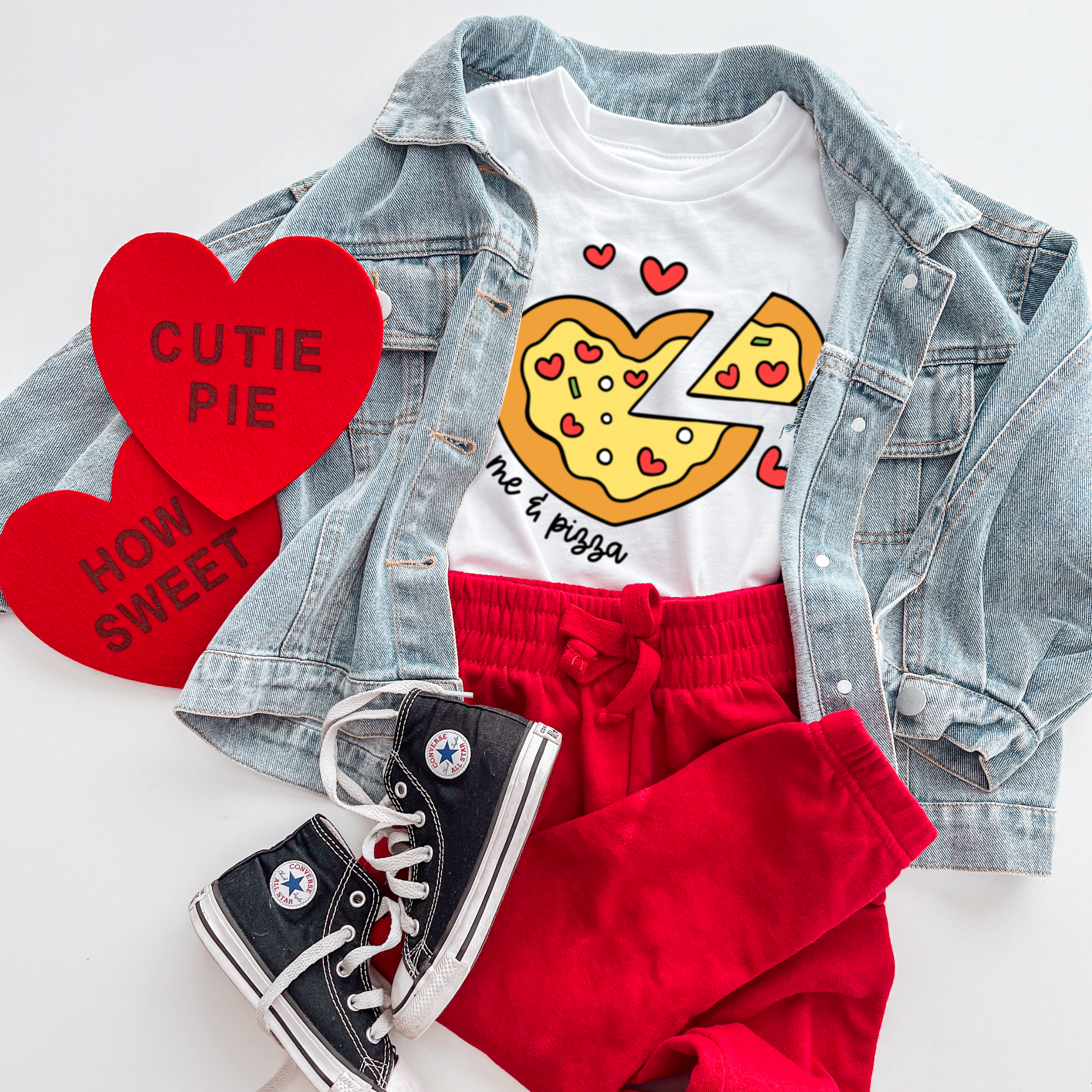White t-shirt with pizza graphic, red sweatpants, denim jacket, and black sneakers on a white background.